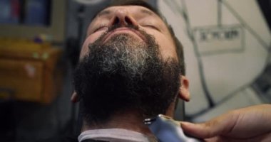 Berber dükkanında saç kesimi sakallı. Profesyonel bir kuaför, müşterisinin sakalını siyah saç boyasıyla boyar. Berber dükkanındaki yakışıklı adam bir kuaförde sakalını kesiyor..