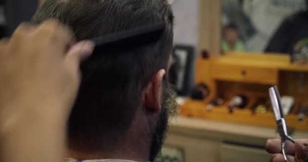 Un peluquero profesional hace una tira de pelo y barba al cliente. Barba cortada en la peluquería. Un hombre guapo en una barbería se afeita la barba en una barbería. — Vídeos de Stock