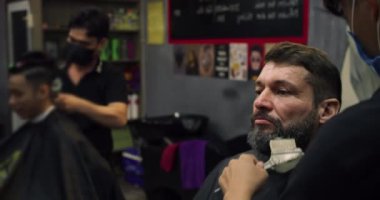 Berber dükkanındaki yakışıklı adam bir kuaförde sakalını tıraş ediyor. Profesyonel bir kuaför, müşterisinin sakalını siyah saç boyasıyla boyar. Berber dükkanında saç tıraşı olmuş..