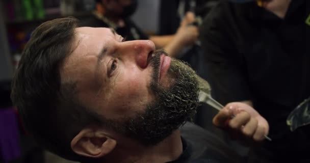 Un coiffeur professionnel se rase la barbe avec une tondeuse à cheveux. Coupe barbe avec lame chez le coiffeur. Beau homme se faire raser la barbe dans un studio de coiffure. — Video