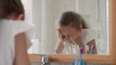 Portre mutlu genç kız yüzünü banyoda yıkıyor ve gülümsüyor. Çocuklar günlük sağlık hizmetleri rutini. Kafkasyalı küçük bir kız aynaya bakıp yüzünü yıkar. Evinde yıkanır. Yaşam tarzı.