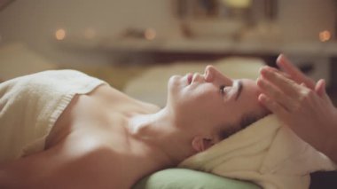 Sağlık hizmeti vücut masajı spa konsepti. Genç, beyaz, güzel bir kadın güzellik salonundaki masaj terapistinden yüz masajı yaptırıyor..