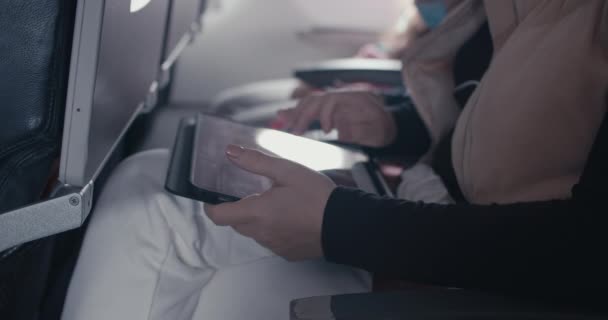 Μια νεαρή γυναίκα με καυκάσια εμφάνιση κάνει μια πτήση σε ένα αεροπλάνο, ένας έφηβος χρησιμοποιεί ένα τηλέφωνο σε ένα αεροπλάνο, περπατά μέσα από εικόνες, μηνύματα, ανοίγει μια εφαρμογή. — Αρχείο Βίντεο
