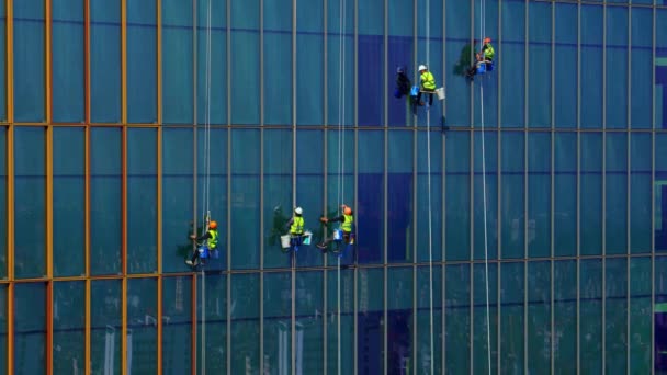 Vijf arbeiders in beschermende covid maskers en blauwe en gele werkkleding wassen de buitenramen van een zakelijke wolkenkrabber - industriële bergbeklimming. Grote mensen wassen ramen. Reinigingsconcept — Stockvideo