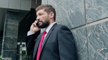 Sokakta bir adam cep telefonuyla konuşuyor. Bir metropolün finans bölgesinde lüks giysiler içinde ciddi bir orta yaşlı işadamı görüşmeler için cep telefonu kullanıyor. 4K