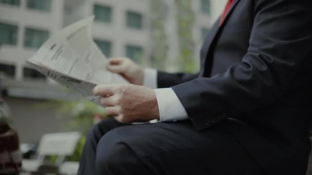 Homme d'affaires aîné en costume cher avec une belle barbe en veste bleue noire s'assoit sur un banc dans le parc et lit un journal. — Video