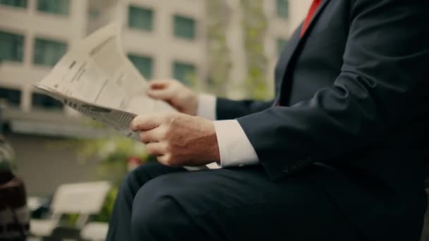 Homme d'affaires aîné en costume cher avec une belle barbe en veste bleue noire s'assoit sur un banc dans le parc et lit un journal. — Video
