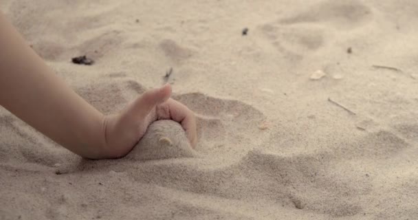 Kindermädchen in Großaufnahme, die Sand durch die Finger schütten, Zeitlupe am Strand mit Sonnenaufgang und blauem Himmel. Kleines Kind spielt bei Sonnenaufgang oder Sonnenuntergang mit Sand. — Stockvideo