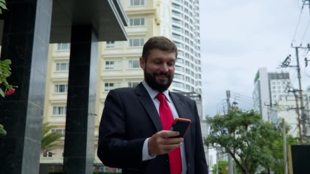 A business man texting phone in the street. A serious middle-aged businessman in luxurious clothes in the financial district of a metropolis uses a mobile phone for negotiations. 4 — Stock Video