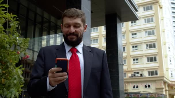 한 사업가 가 길거리에서 문자를 보내고 있었습니다. 대도시 금융 지구에서 호화 로운 옷을 입은 진지 한 중년 사업가가 협상을 위해 휴대폰을 사용 한다. 4. — 비디오