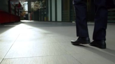 Pahalı takım elbiseli bir işadamı elinde evrak çantasıyla güneşli yaz gününde şehir caddesinde ağır çekimde yürüyor. Kavram işadamı, teknoloji, iletişim, başarı.