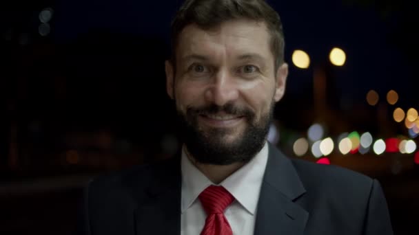 Portrait of a Successful male in an expensive suit, a handsome bearded senior businessman in the evening stands on the streets of the city next to a business building and looks at the camera, smiling. — стоковое видео