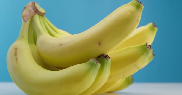 Κίτρινες όμορφες ώριμες μπανάνες ξαπλωμένες στο τραπέζι σε μπλε φόντο. Οι ώριμες μπανάνες κάνουν κύκλους. Ενδιαφέρουσα γωνία, πλάνα αρχείου. — Αρχείο Βίντεο