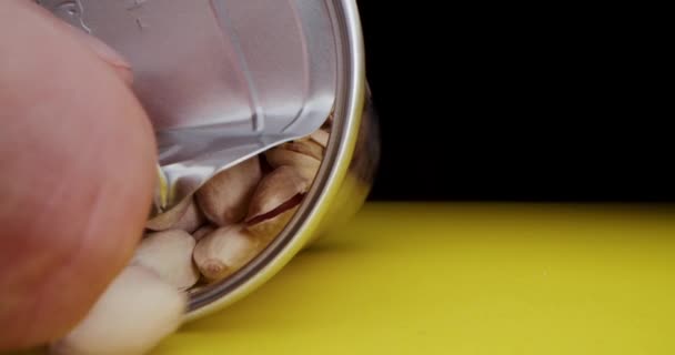 Macro lens, Macro shot, a womans hand opens a can of pistachios in a beautiful light on a black and yellow background, falling into the camera on pistachios. — стоковое видео