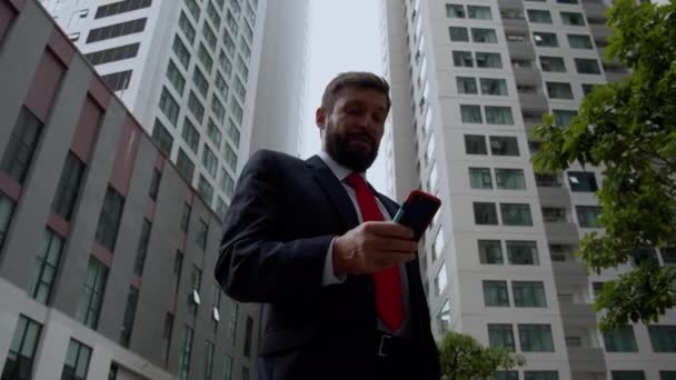 Egy üzletember sms-ezik az utcán. Egy komoly középkorú üzletember luxusruhákban egy nagyváros pénzügyi negyedében mobiltelefont használ a tárgyalásokhoz. 4. — Stock videók