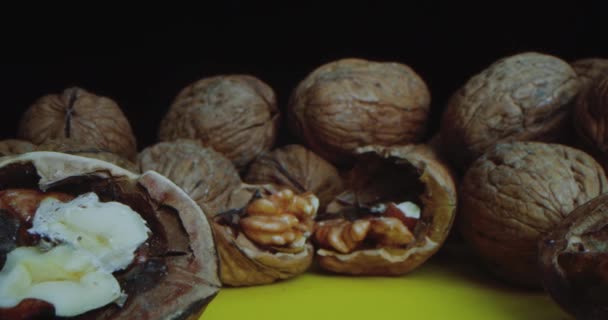 Primer plano de nueces que yacen sobre una mesa amarilla sobre un fondo negro. Primer plano de la cámara de viaje a lo largo de las tuercas acostadas lo más cerca posible de la nuez picada. — Vídeos de Stock