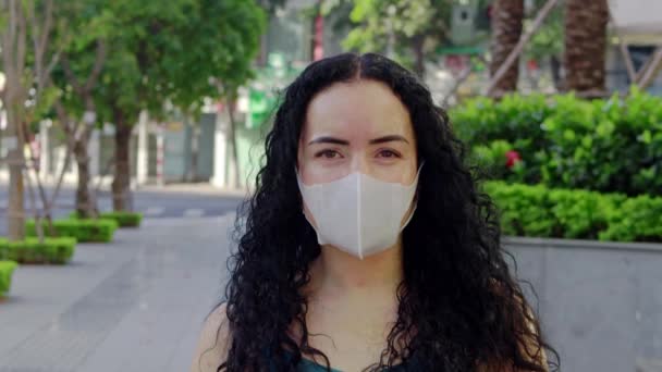 의료용 마스크를 쓰고 빈 거리와 도시 배경에 카메라를 보고 있는 성인 여성의 근접 사진입니다. 세균성 감염, 코로나 바이러스 , Covid 19. 코로나 바이러스 — 비디오