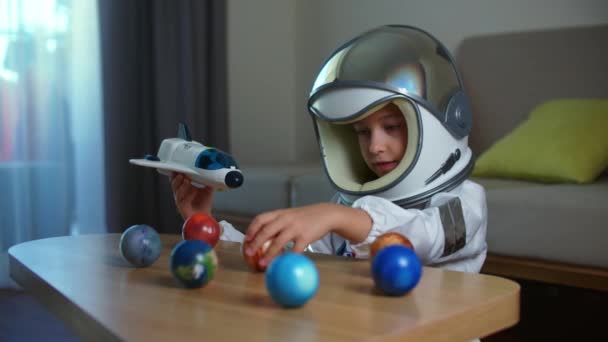 Çocuk evde bir astronotla oynuyor, 8-9 yaşlarındaki oyuncak uzay giysili komik bir kızın komik bir portresi, gülümseyen bir çocuk, bir uzay roketi fırlatıyor, yakın plan, uzayda seyahat eden bir pilot. Mutlu çocukluk — Stok video