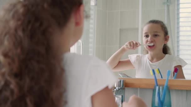 Ritratto felice carino giovane ragazza adolescente lavarsi i denti in bagno e sorridere. routine sanitaria quotidiana dei bambini. Ragazzo caucasico con un dente bianco che si guarda allo specchio isolato a casa. Stile di vita. — Video Stock