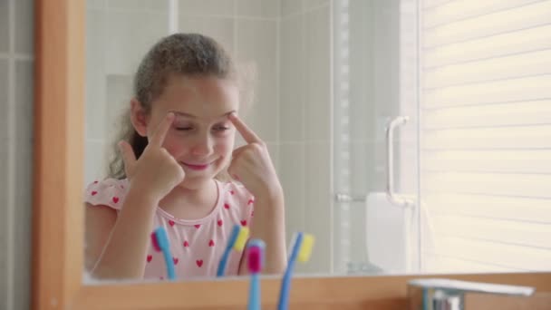 Πορτρέτο ενός ευτυχισμένου χαριτωμένο νεαρό κορίτσι εφηβεία γλιστρά μπροστά από τον καθρέφτη, κάνει ένα αστείο πρόσωπο στο μπάνιο και χαμόγελα.Καθημερινή θεραπευτική αγωγή υγείας για τα παιδιά.Καυκάσιο κοριτσάκι με κοιτάζοντας στον καθρέφτη. — Αρχείο Βίντεο