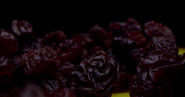 Macro shot in black key close-up of dry grapes of black raisins lying on a table against a black background. Macro close-up of raisins. Interesting angle, stock footage. — Stock videók