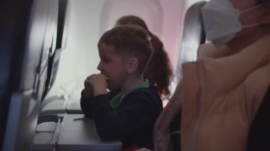 Küçük çocuk uçakta ailesiyle uçarken hamburger yiyor ve yemeğin tadını çıkarıyor. Ailesi olan çocuklar uçakta uçar, çocukluk yolculuğu konsepti..