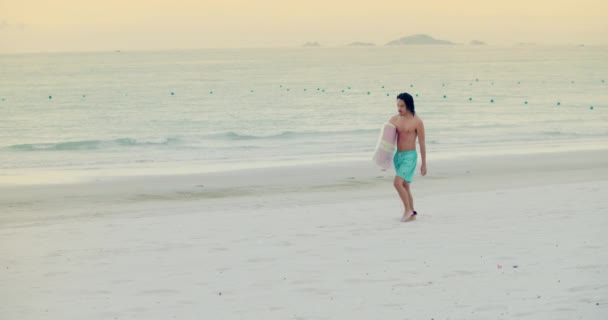 Um desconhecido asiático desportista surfista caminha com uma prancha de surf. O atleta está arando do mar, indo dos passeios nas ondas após o surfão.Província de Han Hoa, Vietnã, 27 de setembro de 2021 — Vídeo de Stock