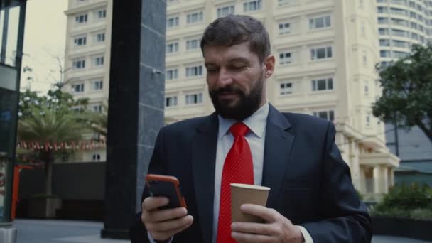 Homme d'affaires avec téléphone, buvant du café. Homme barbu élégant sérieux dans des vêtements astylish textos sur smartphone personnel, la lecture d'un journal sur une tablette en plein air. — Video