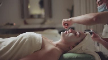 Spa yatağında uzanıp yüz masajı yapan rahat bir kadın lüks spa merkezindeki masör, spa merkezinde yüz maskesi takan bir kız. Sağlık, stres atma ve gençleştirme kavramı.