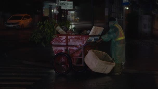 A cleaning oldman on the street removes garbage. Cleanliness and order in the yard depends on the janitor during quarantine.Rainwater flows on the road and fall into the metal hatch with holes drain. — Stock Video