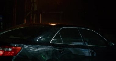 Rain falls on a parked car, it rains and drops of water drip onto the roof of the car. It rains heavily at night.