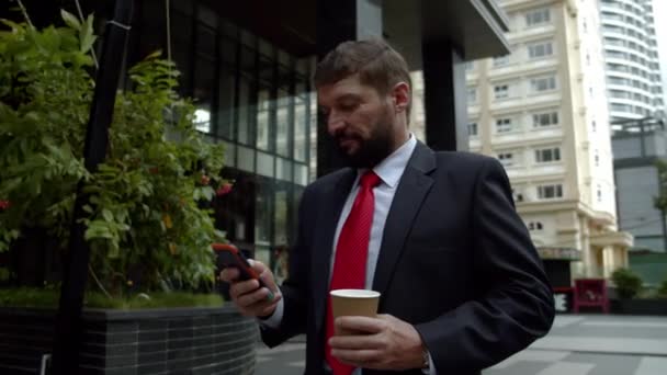 Egy férfi beszél egy mobilon az utcán. Egy komoly középkorú üzletember luxusruhákban egy nagyváros pénzügyi negyedében mobiltelefont használ a tárgyalásokhoz. 4K — Stock videók