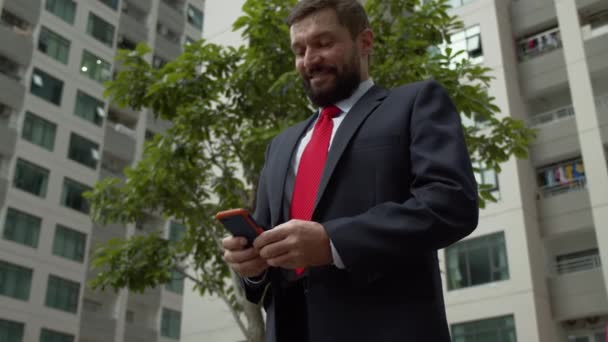 Businessman with phone, drinking coffee. Serious elegant bearded man in astylish clothes texting on personal smartphone, reading a newspaper on a tablet computer in outdoors — 图库视频影像