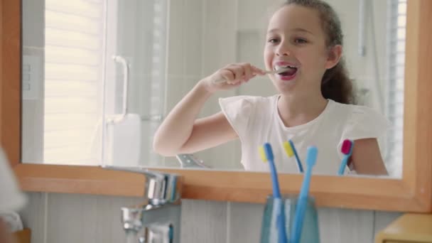 Portré boldog aranyos fiatal tizenéves lány fogmosás a fürdőszobában és mosolygós. Gyermekek napi egészségügyi rutin. Fehér gyerek fehér foggal, otthon elszigetelt tükröt néz. Életmód. — Stock videók
