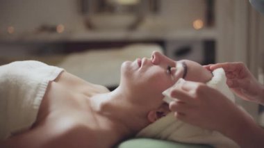 Sağlık, stres atma ve gençleştirme konsepti. Spa yatağında uzanıp spa tedavisi gören rahat bir kadın. Spa merkezindeki masör, spa merkezinde yüz maskesi takan bir kız..