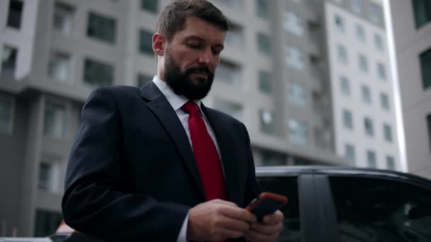 Homme d'affaires sérieux d'âge moyen en vêtements de luxe dans le quartier financier d'une métropole utilise un téléphone portable pour les négociations.Homme d'affaires textos téléphone dans la rue. — Video