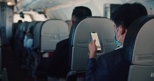Αντιπροσωπεία Ασιατών επιχειρηματιών που φορούν αλεξίσφαιρες μάσκες πετούν με αεροπλάνο σε οικονομικό φόρουμ κατά τη διάρκεια πανδημίας, ένας άνδρας χρησιμοποιεί τηλέφωνο σε αεροπλάνο, Βιετνάμ, Ανόι, 28 Νοεμβρίου 2021. — Αρχείο Βίντεο