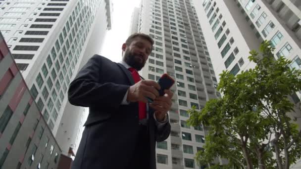 Homme d'affaires avec téléphone, buvant du café. Homme barbu élégant sérieux dans des vêtements astylish textos sur smartphone personnel, la lecture d'un journal sur une tablette en plein air — Video