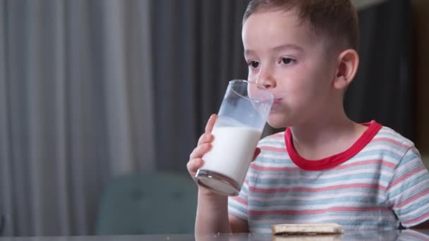 Retrato niño caucásico feliz Niño feliz que come pan y bebe leche de un vaso por la noche mientras está sentado en la cocina en casa. Concepto de infancia feliz disfrutando pasar tiempo en casa. — Vídeos de Stock