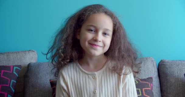 Portrait Funny little girl smiling child looking at camera are sitting on the couch at home, cute kid child with pretty face sitting on sofa. Concept of a happy childhood. — Stock Video