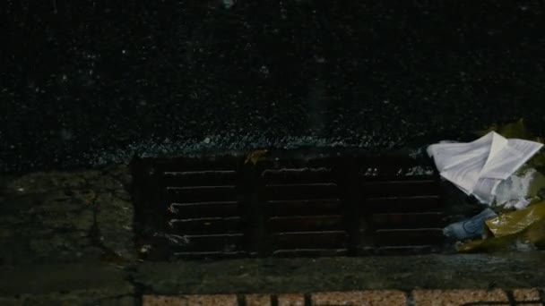 歩道に降る雨春の雨が降っていると水の滴が水たまりに滴下されています排水路を流れる雨水道路上を流れ、穴の排水と金属ハッチに落ちる. — ストック動画