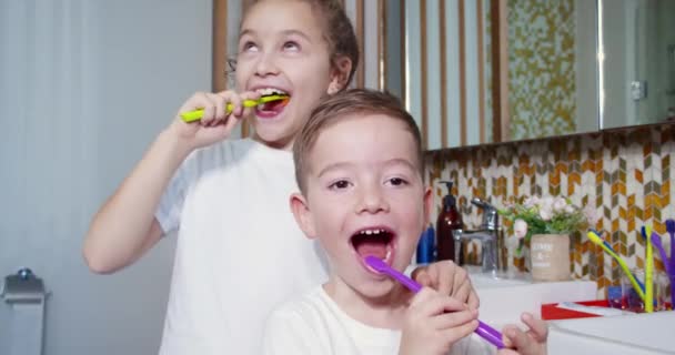 Barn daglig sjukvård rutin. Porträtt glada söta små barn borsta tänderna i badrummet och leende. Kaukasiska barn borstar titta på spegeln hemma. Livsstil. — Stockvideo