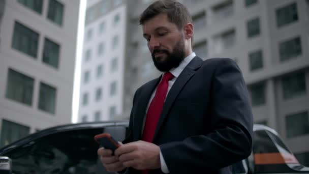 在大都市的金融区，一位穿着华丽服装的严肃的中年商人用手机进行谈判。商人在街上发短信. — 图库视频影像