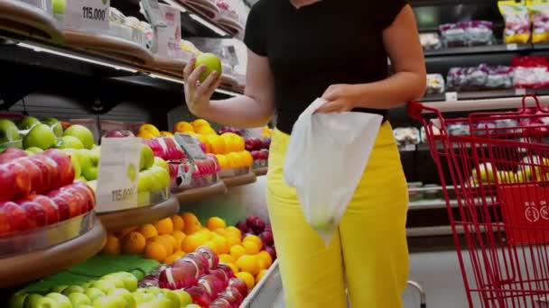 한 젊은 여자가 슈우퍼 마아 킷 의 식료품 점에서 서 무게가 나가는 자루에 사과를 집고 있다. — 비디오