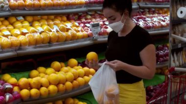 Coronavirüs salgınından maske takan genç bir kadın bir süpermarketin market bölümünde duruyor. Meyve alıyor, yeşil elma..