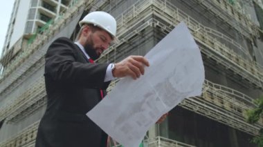 Oradaki inşaat sahasında, çizimlere göre çok katlı binaların hangi aşamasında inşa edildiği kontrol edilen bir inşaat mühendisi, tasarımcı var. Mühendis şemaya bakar ve yapıyı tamamlar.