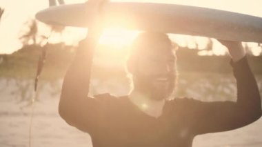 O yaştaki son sınıf sporcusu plajda sörf tahtasıyla gezer. Emekli bir sporcu denize açılır, dalgalara sörf tahtası ile biner..