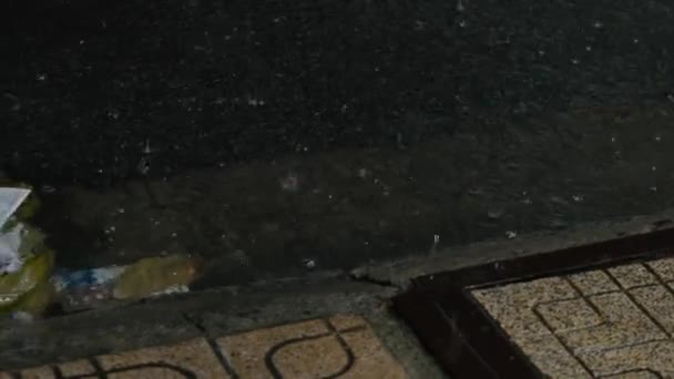 Regenwater dat door een afvoer stroomt Regenwater stroomt over de weg en valt in het metalen luik met gaten in de afvoer. Regen valt op trottoir De lenteregen valt en druppels water druppelen in plassen — Stockvideo