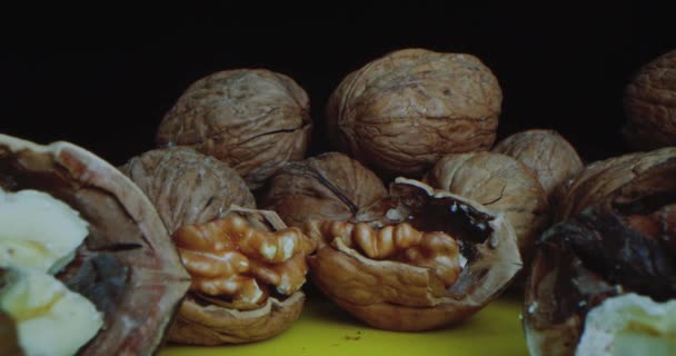 Primer plano de nueces que yacen sobre una mesa amarilla sobre un fondo negro. Primer plano de la cámara de viaje a lo largo de las tuercas acostadas lo más cerca posible de la nuez picada. — Vídeos de Stock