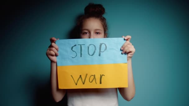 Verontrust Oekraïense arme peuter bang meisje kind dakloze protesteren oorlog conflict verhoogt banner met inscriptie massage tekst No War op blauwe achtergrond. Vrede, stop agressie, kind tegen Russische oorlog — Stockvideo